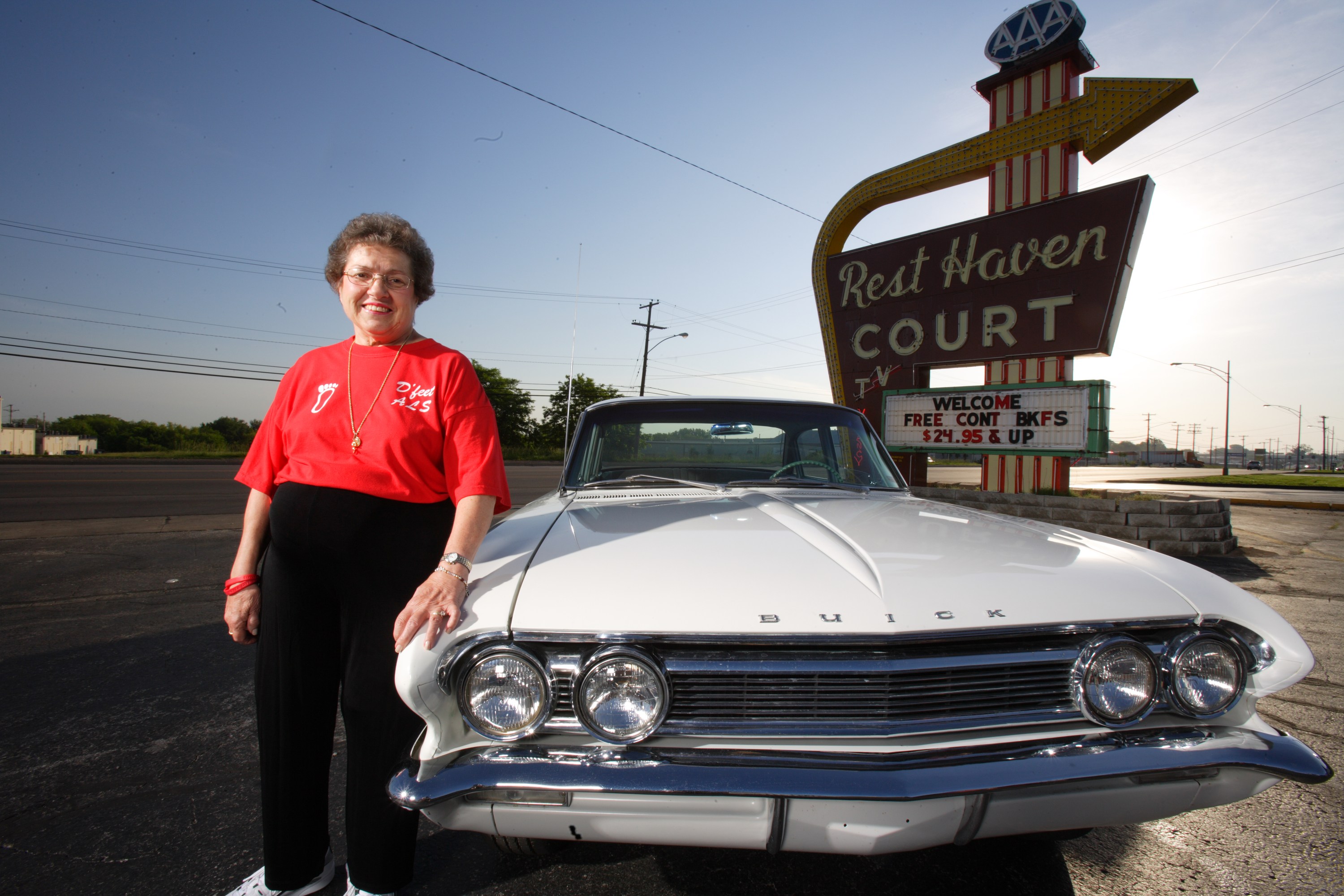Deanna Brekken in a D'feet ALS shirt beside a classic Buick and the Rest Haven Court sign on Route 66