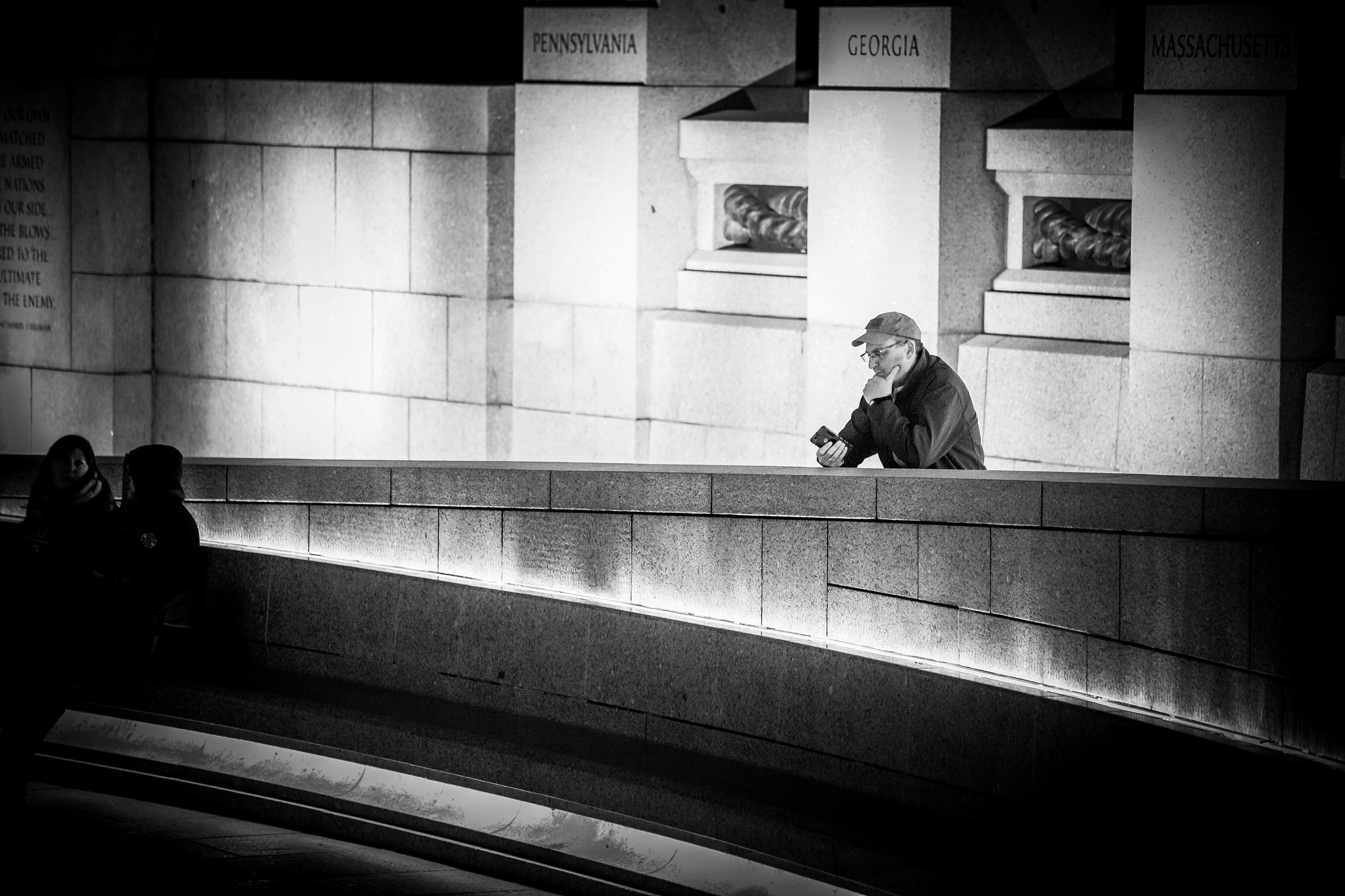 David J. DeJonge pauses at the National World War II Memorial at night beneath illuminated state pillars