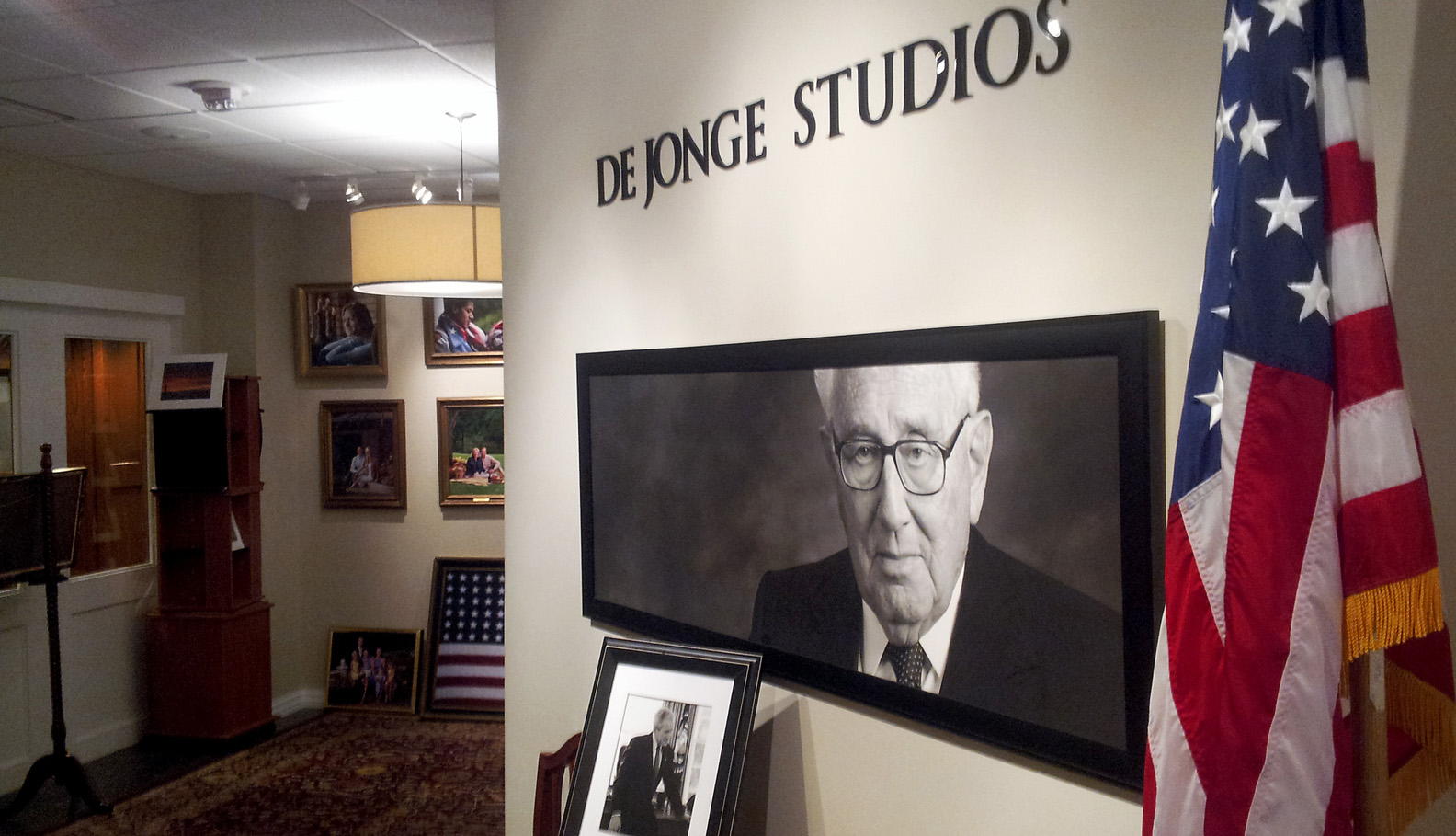 Wide view of the light-walled DeJonge Studio gallery at the Amway Grand Plaza Hotel with framed portraits and an American flag