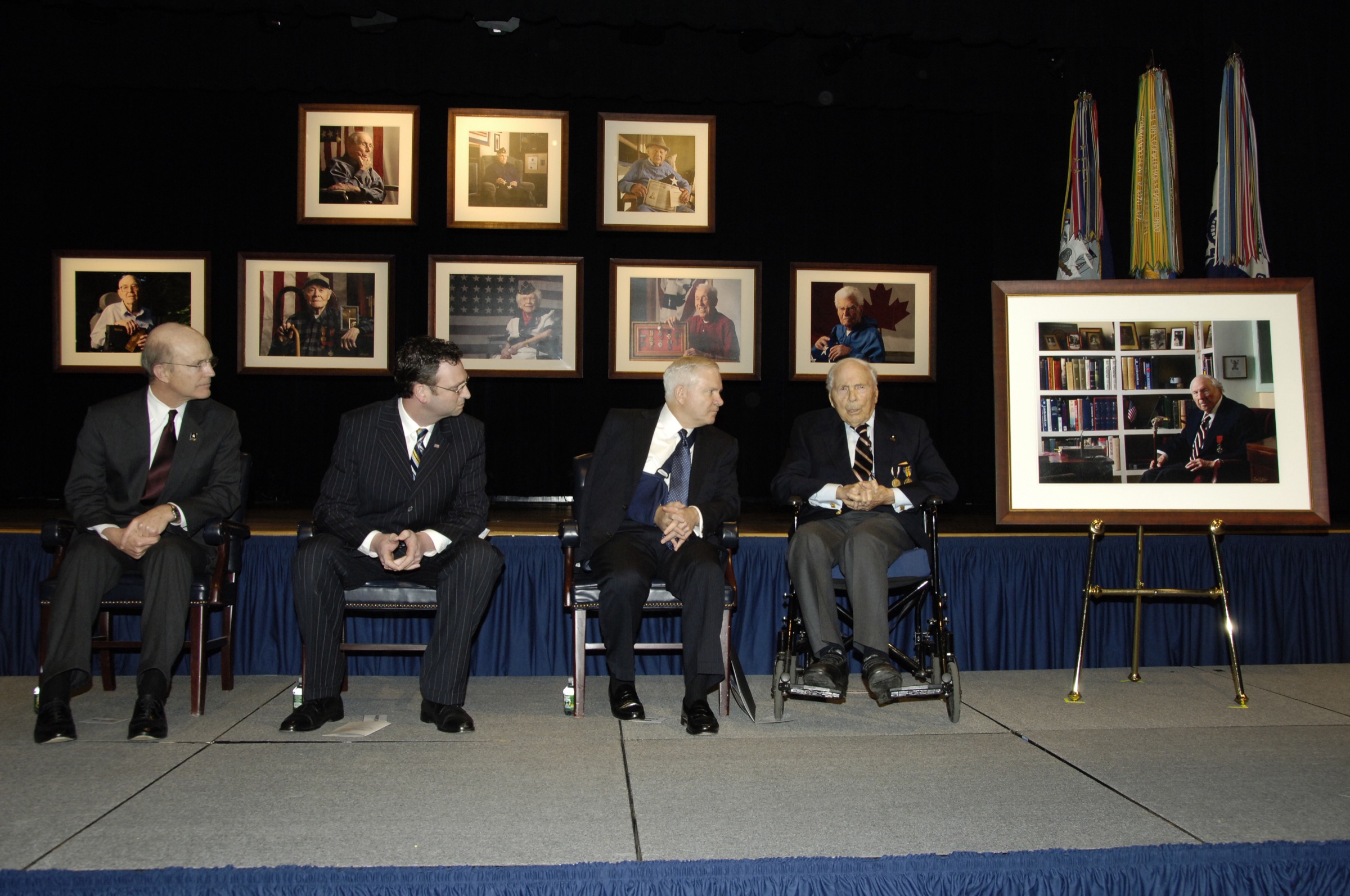 Secretary of the Army Pete Geren, David DeJonge, Secretary of Defense Robert Gates, and Frank Buckles seated before eight veteran portraits with Buckles's ninth portrait on an easel