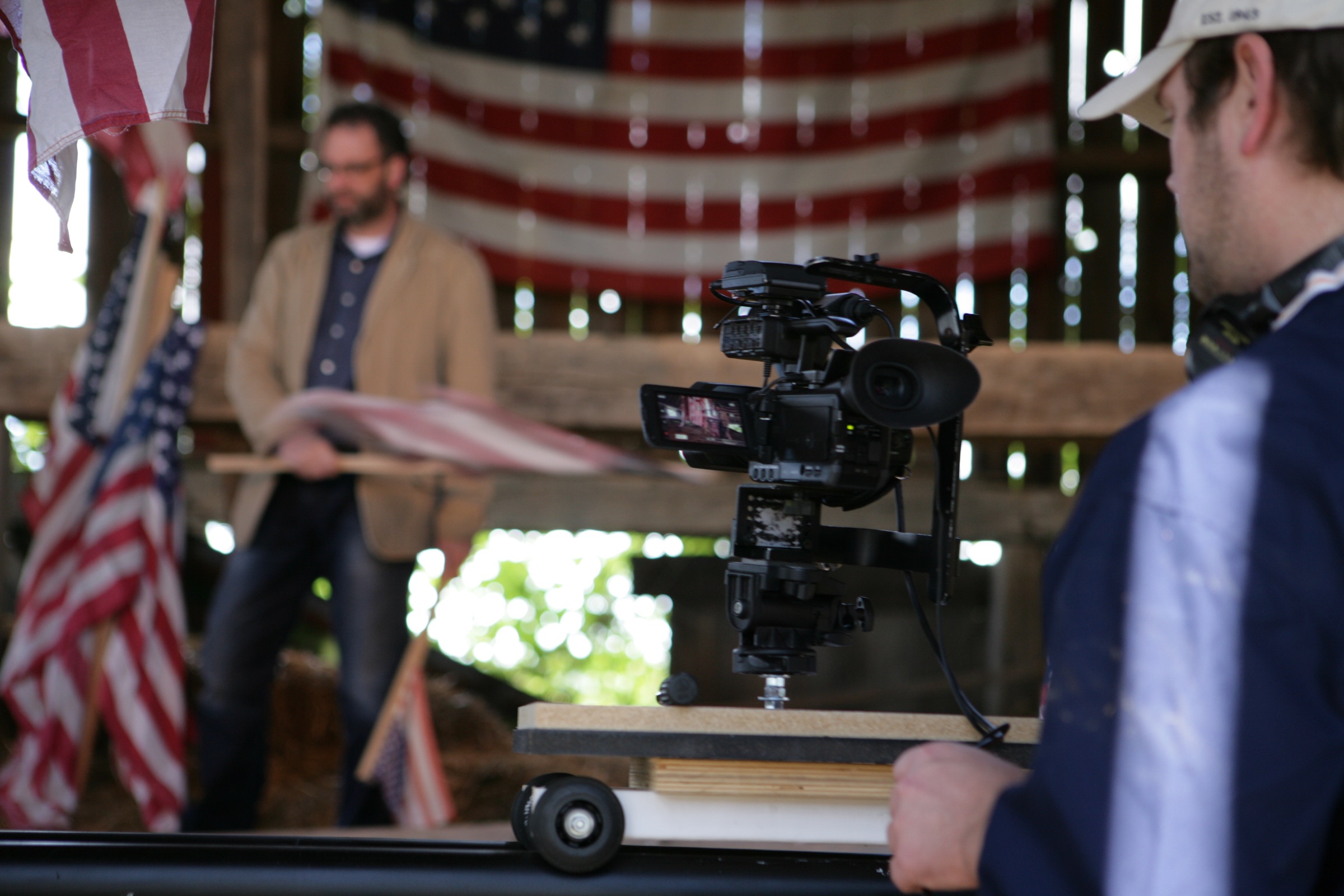 Cinema camera on a slider filming David DeJonge as he works among the flags in the barn