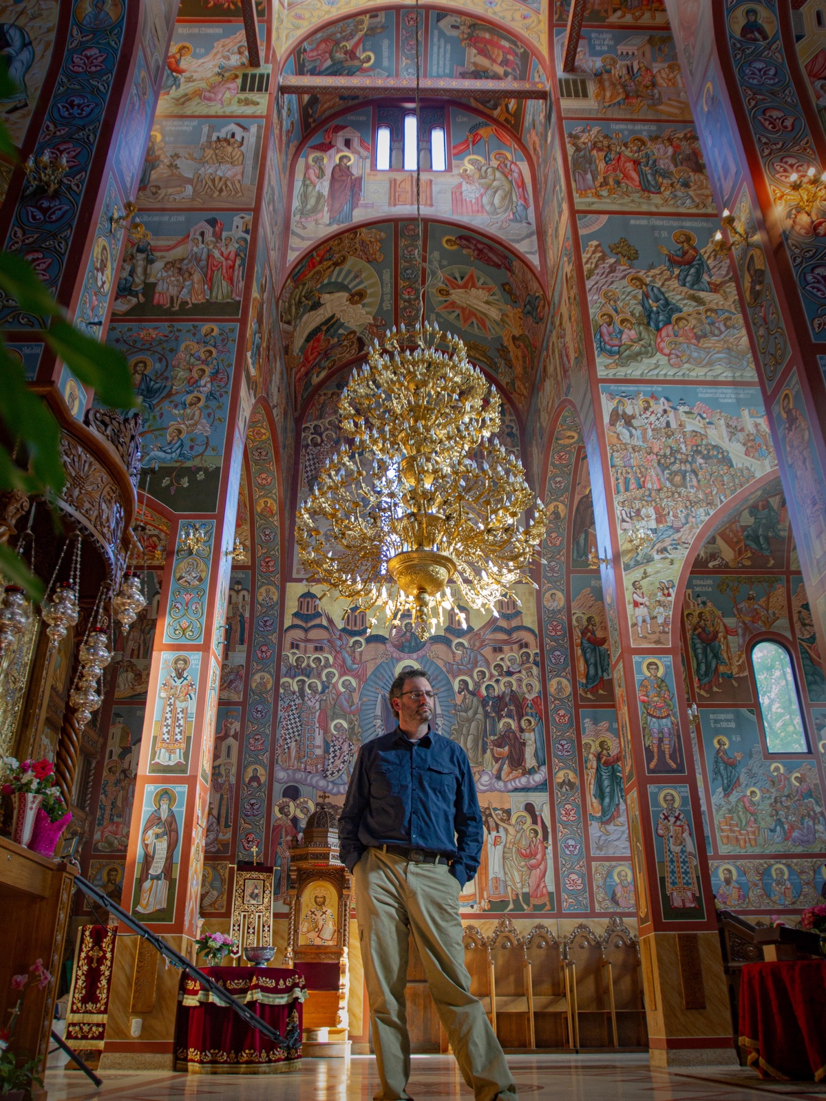 David J. DeJonge standing beneath a monumental chandelier and wall of icons inside New Gracanica Monastery